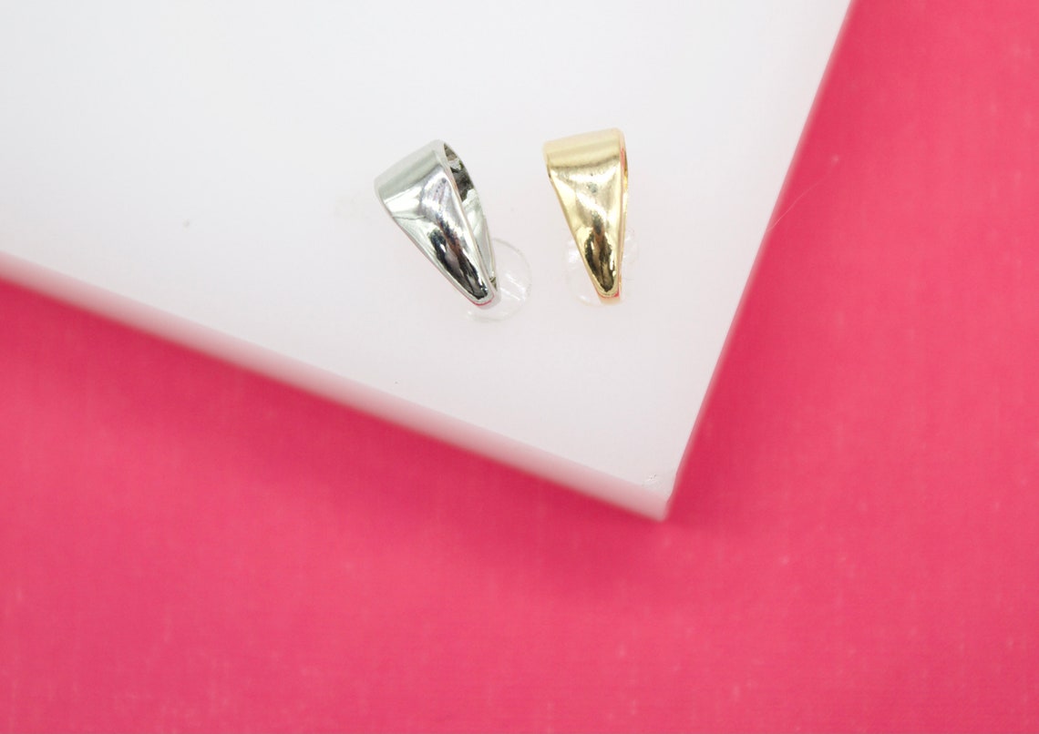 A silver and a gold pinch bail rest on a white display block against a vibrant pink background.