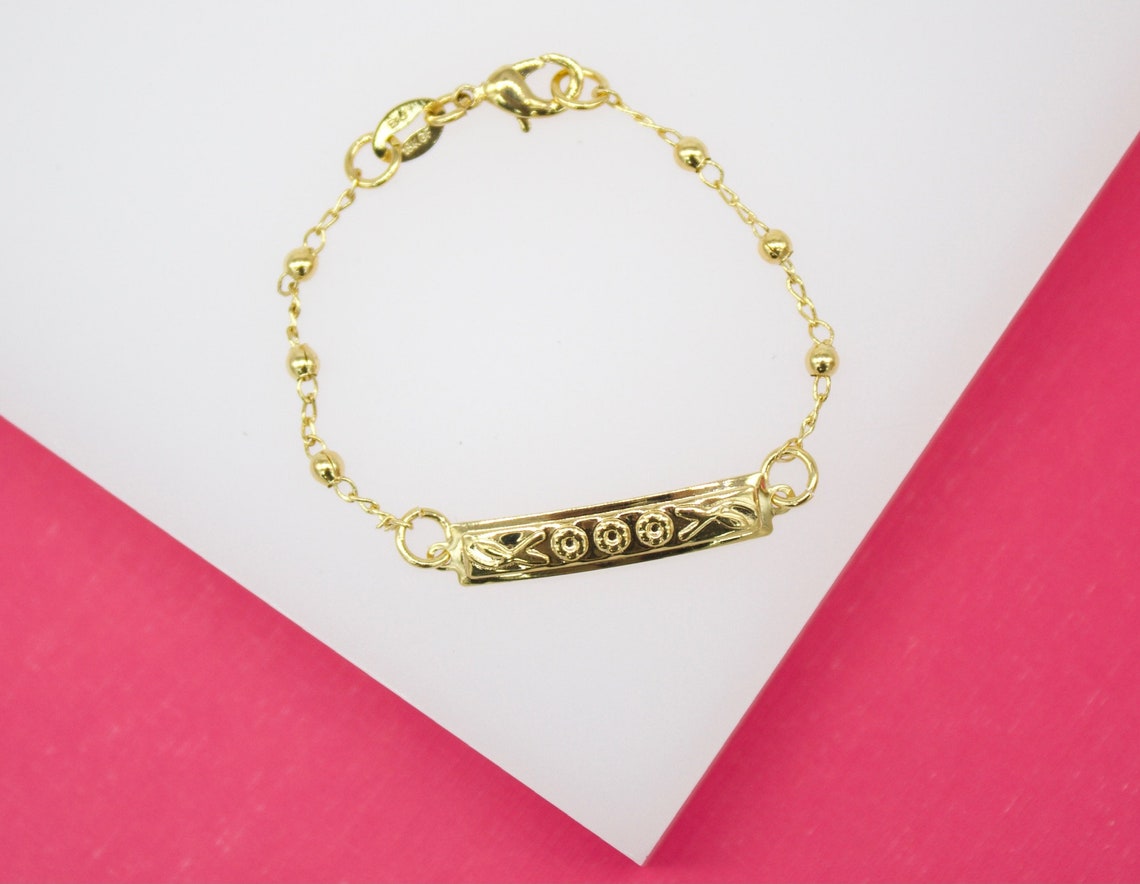 A delicate gold ID bracelet rests on a white and pink display surface.