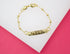 A delicate gold ID bracelet rests on a white and pink display surface.