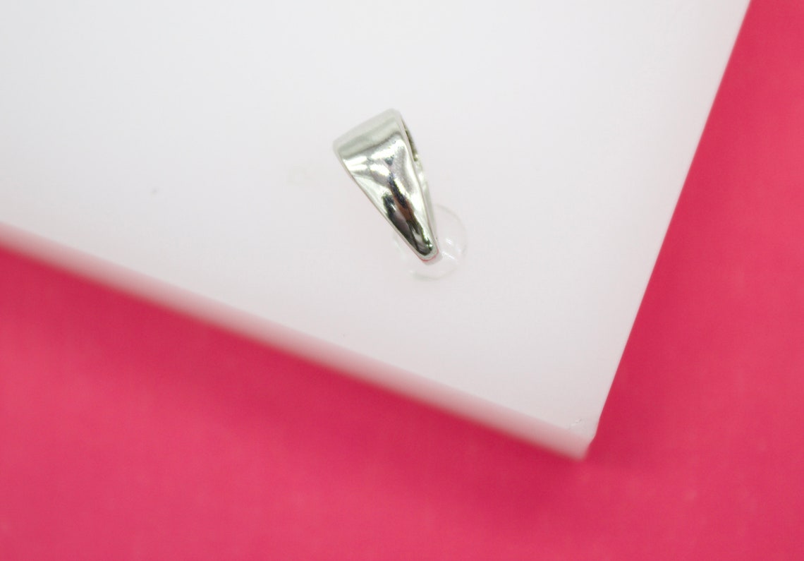 A shiny silver bail connector rests on a white display surface against a bright pink background.