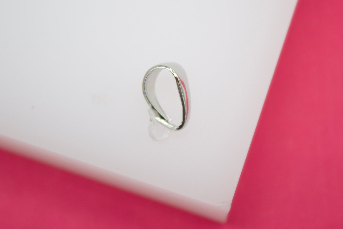 A sleek silver bail sits on a white display block against a vibrant pink background.