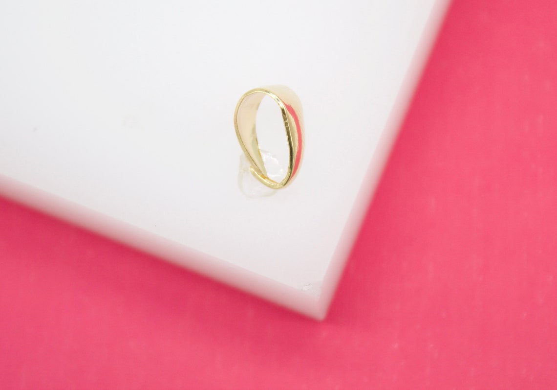 A polished gold bail rests on a white display surface against a vibrant pink background.