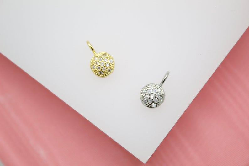 A gold and silver pave disc pendant sparkle on a white display surface.