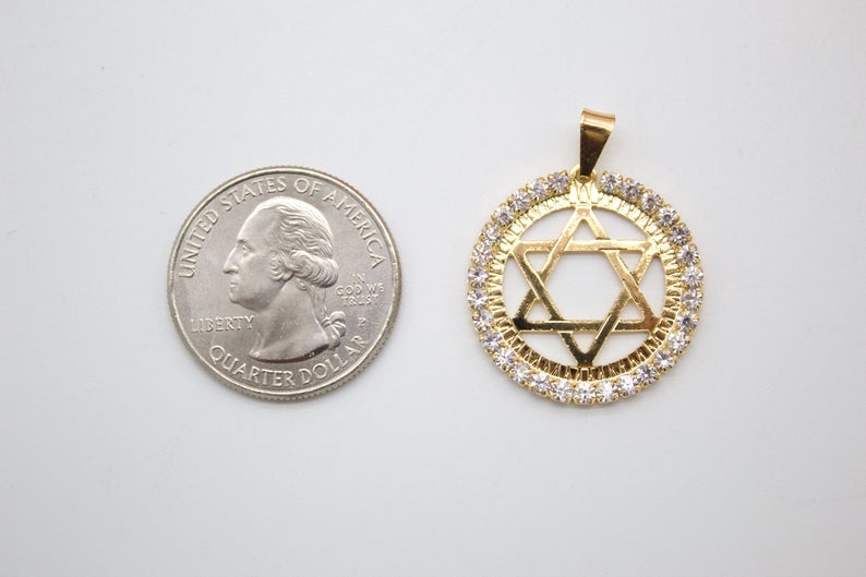 A gold Star of David pendant encrusted with sparkling crystals rests beside a US quarter coin on a white surface for size comparison.