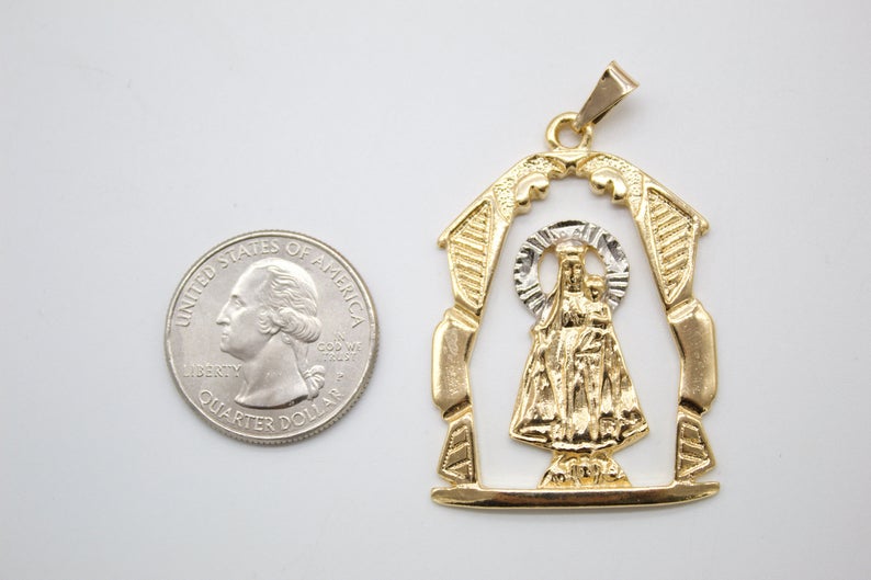 A gold pendant featuring Our Lady of San Juan de los Lagos rests beside a US quarter for scale.