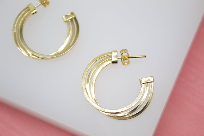 A pair of glossy gold triple-band hoop earrings rests against a white display surface.