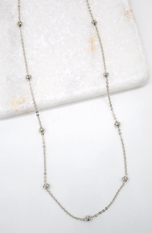 A delicate silver station necklace featuring intricately filigree beads displayed on a white marble surface.