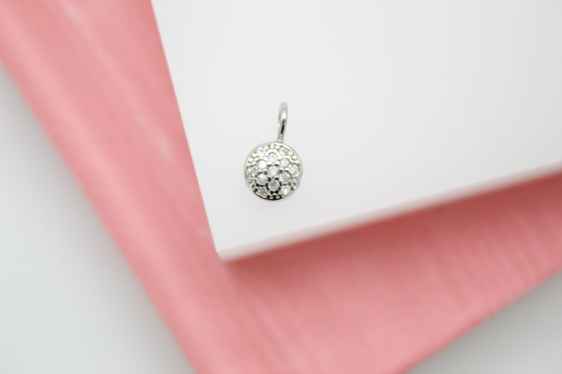 A small silver diamond pendant rests on a white display surface against a pink background.