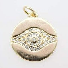 A round gold evil eye pendant sparkles with embedded diamonds against a plain white background.