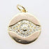 A round gold evil eye pendant sparkles with embedded diamonds against a plain white background.