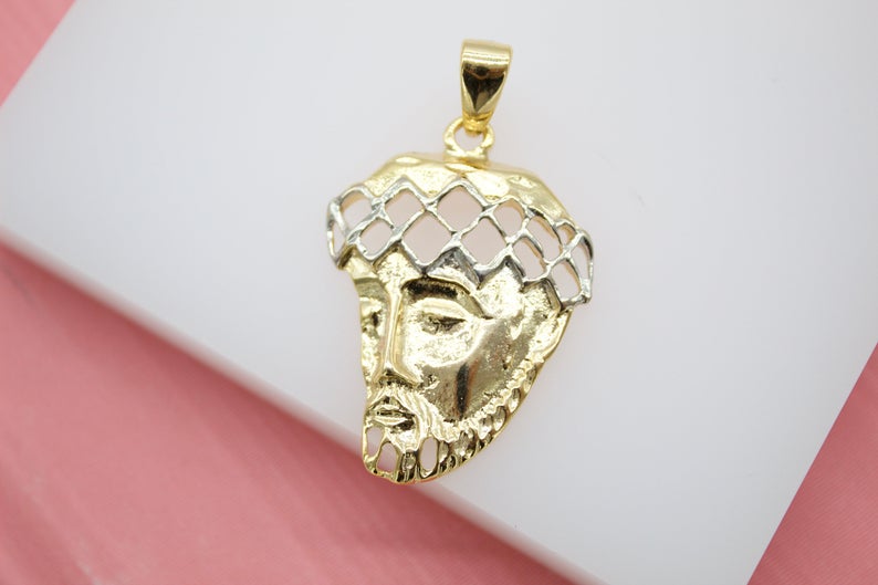 A detailed gold and silver Jesus Christ head pendant rests against a white display surface.