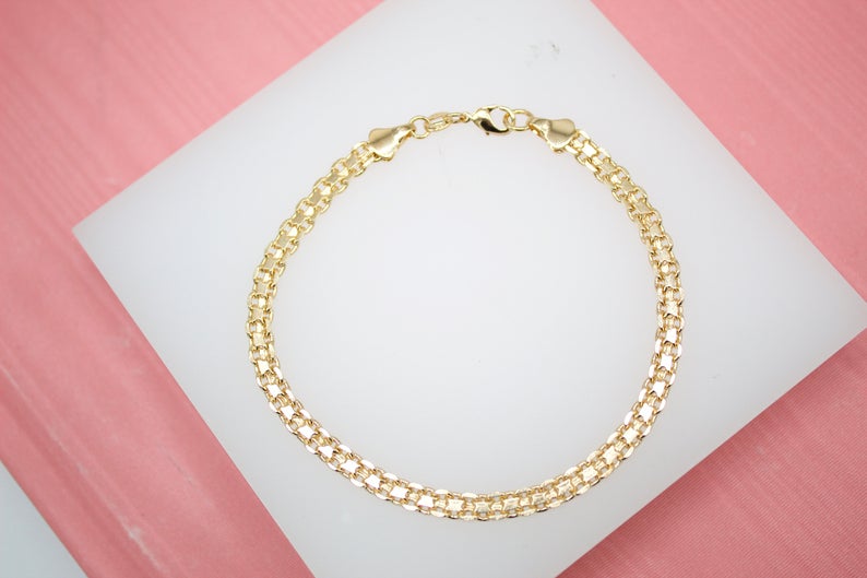 A polished gold link bracelet rests on a white display stand against a pink background.