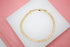 A polished gold link bracelet rests on a white display stand against a pink background.