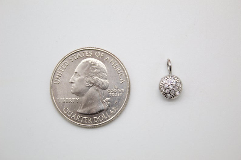 A small diamond-encrusted silver pendant rests beside a US quarter for scale.