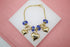 A gold charm bracelet featuring sparkling blue beads and dangling heart charms rests on a white display against a pink background.
