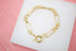 A shiny gold paperclip chain bracelet rests on a white display surface.