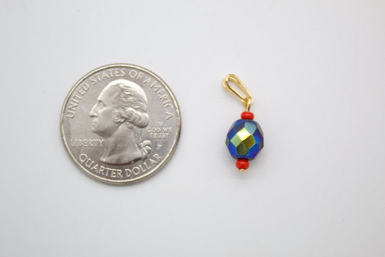 A small, iridescent blue and green crystal bead pendant with red spacer beads sits next to a US quarter coin for scale.