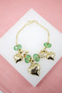A gold charm bracelet features faceted green crystal beads, shiny gold heart charms, and a small elephant figurine, all displayed on a white surface.