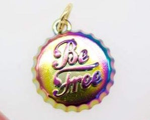 A rainbow-colored metal bottle cap charm features the inspirational phrase "Be Free" engraved in cursive script.