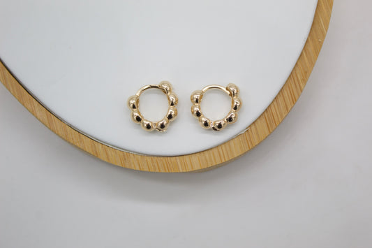 A pair of gold ball-accented huggie hoop earrings rests neatly on a white and wooden display tray.