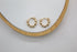 A pair of gold beaded huggie hoop earrings rests on a white and wooden display tray.