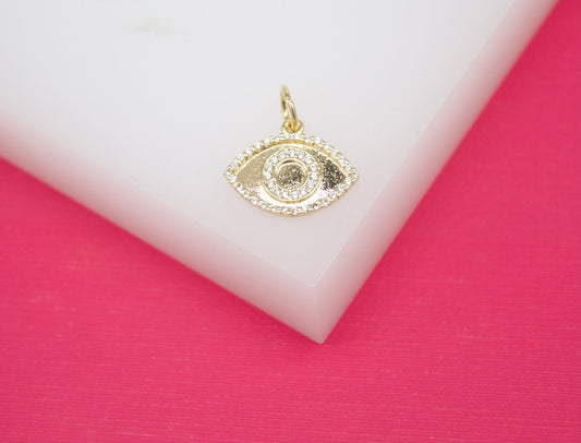 A gold evil eye charm encrusted with sparkling cubic zirconia stones rests on a white and pink display.