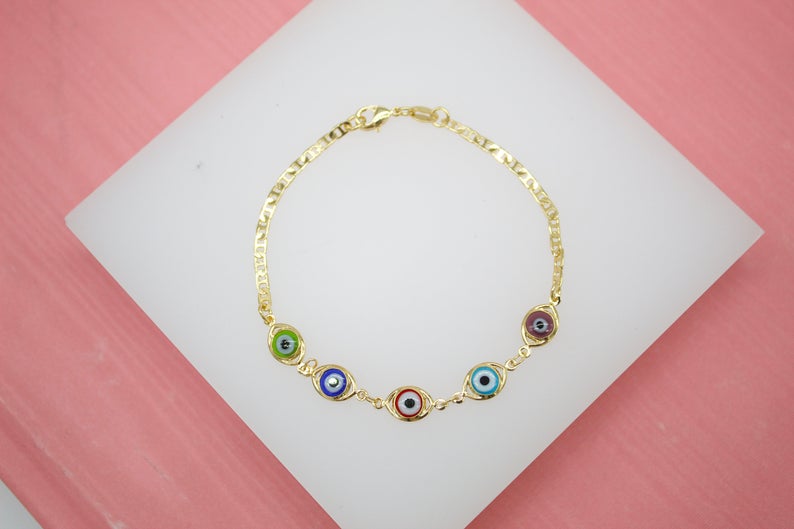 A gold chain bracelet features colorful evil eye charms arranged in a row on a white display surface.