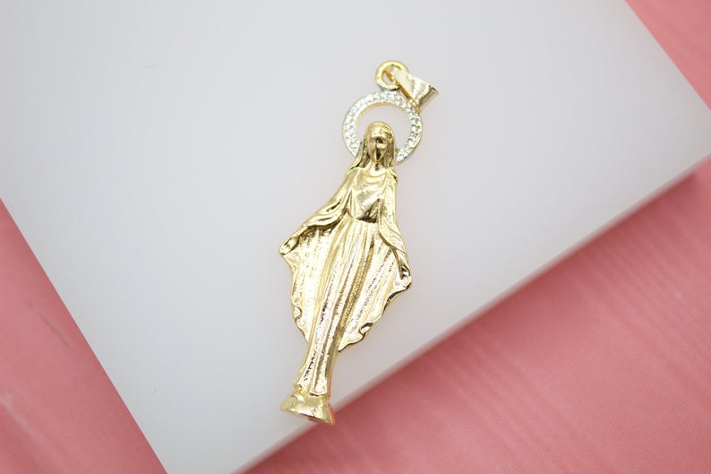 A gold Virgin Mary pendant features a diamond-encrusted halo against a white surface.