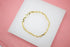 A polished gold link bracelet rests neatly on a white display pad against a soft pink background.