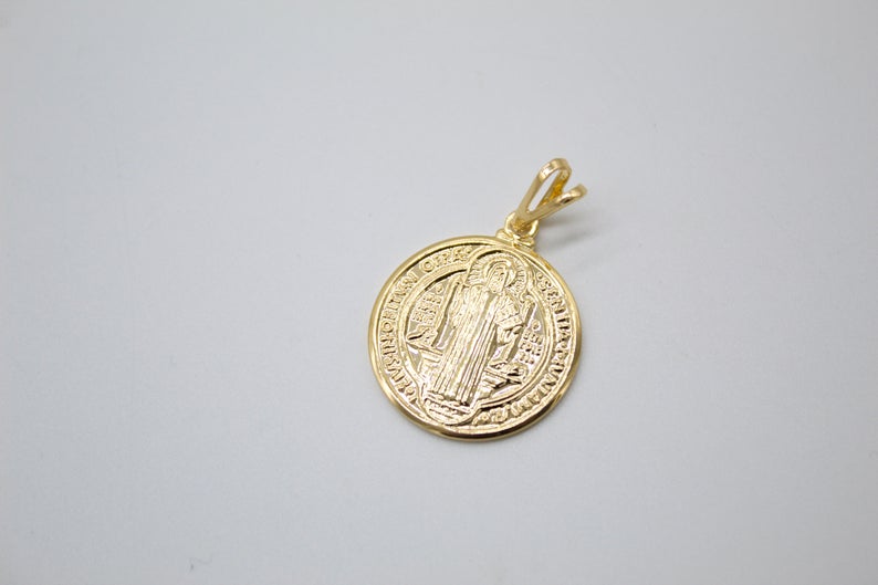 A polished gold Saint Benedict medal pendant rests on a neutral surface.