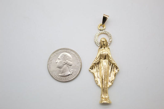 A gold Virgin Mary pendant lies next to a US quarter coin for size comparison.