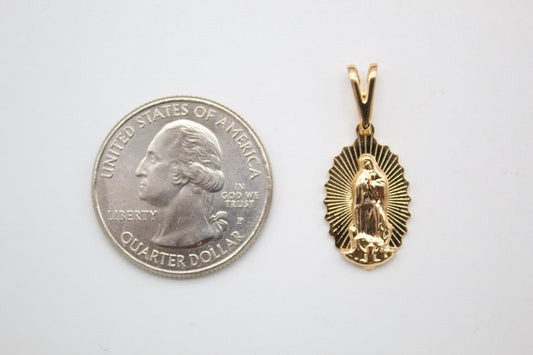 A gold Our Lady of Guadalupe pendant rests next to a US quarter coin for scale.
