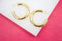 A pair of shiny gold hoop earrings rests on a white display block against a vibrant pink background.