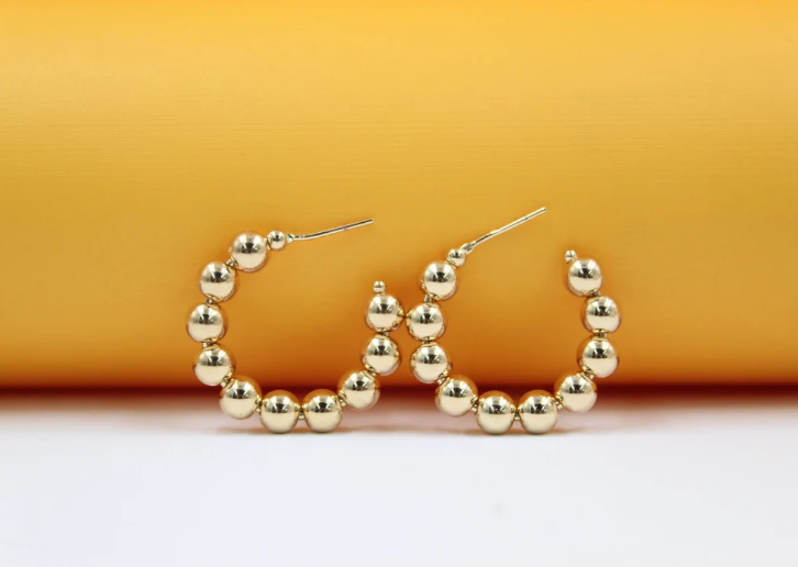 Two gold beaded hoop earrings rest neatly against a vibrant orange and white background.