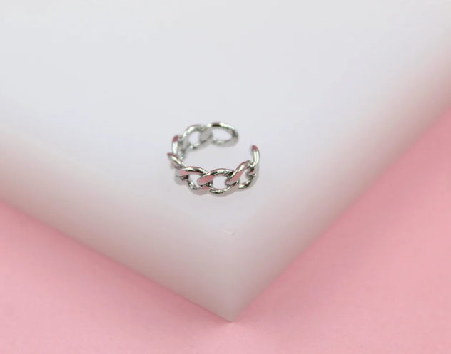 A silver-plated cuban link ear cuff rests on a white display block against a soft pink background.
