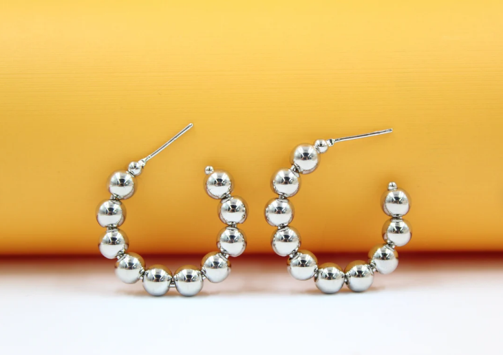 A pair of polished silver bead hoop earrings rests against a vibrant yellow and white background.