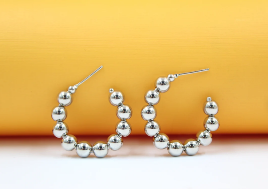 A pair of polished silver bead hoop earrings rests against a vibrant yellow and white background.
