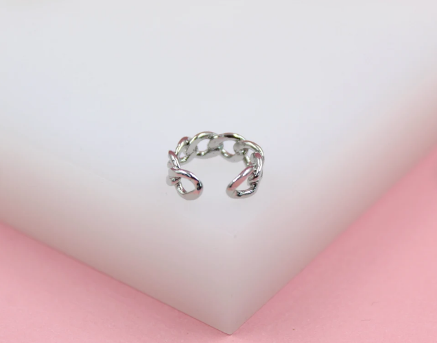 A silver chain-link ear cuff rests centrally on a white display block against a soft pink background.