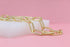 A shiny gold paperclip chain necklace rests elegantly on a white display block against a soft pink background.