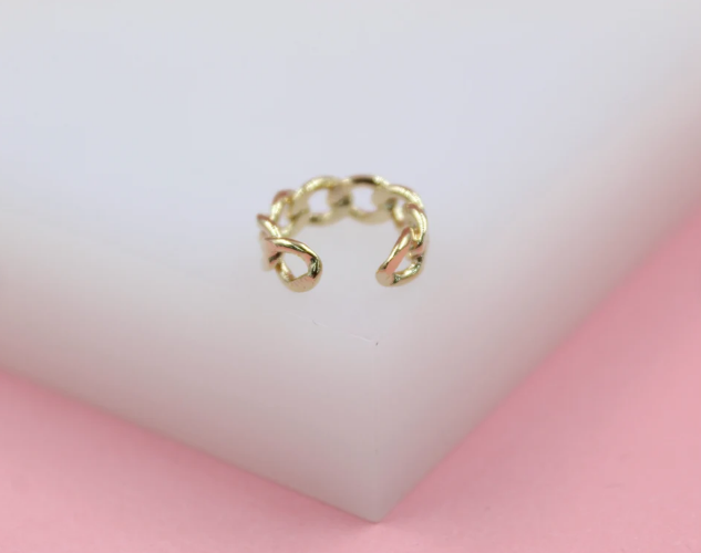 A shiny gold-plated chain-link ear cuff rests on a white display block against a soft pink background.