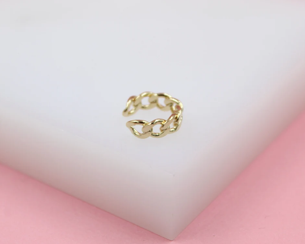 A delicate gold chain-link ear cuff rests on a white display block against a soft pink background.