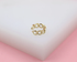 A delicate gold chain-link ear cuff rests on a white display block against a soft pink background.