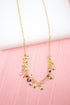 A delicate gold charm necklace featuring dangling metallic discs and colorful beads rests against a pink background.