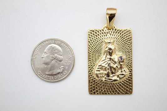 A rectangular gold religious pendant featuring the Virgin Mary rests beside a US quarter coin to demonstrate its size.