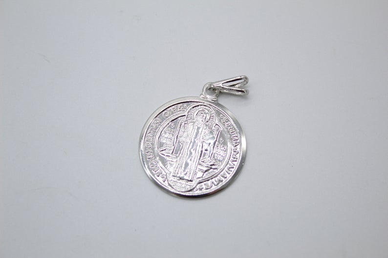 A silver Saint Benedict medal pendant rests on a neutral surface.
