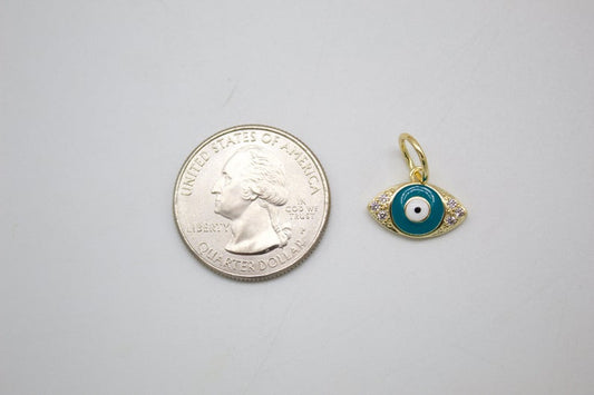 A small gold evil eye charm rests next to a US quarter coin to show its compact size.