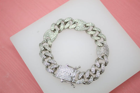 A silver iced-out Cuban link bracelet sparkles on a white display against a pink background.