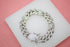 A sparkling diamond-encrusted silver Cuban link bracelet lies displayed on a white surface.