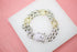A sparkling cuban link bracelet featuring alternating silver-paved links and gold nugget accents rests on a white display surface against a pink background.