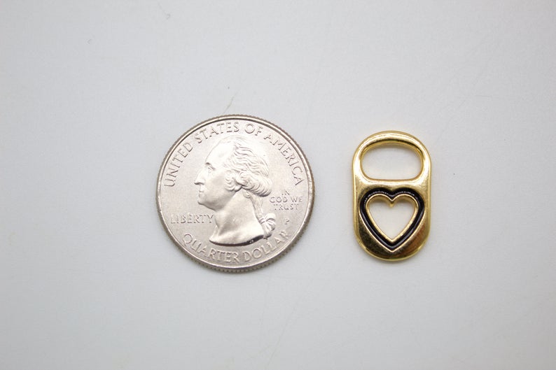 A small gold soda tab charm with a black enamel heart cutout sits next to a US quarter coin for scale.